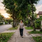 Một người đi bộ chậm trên vỉa hè rợp cây vào chiều muộn, không đeo tai nghe, tập trung vào nhịp thở