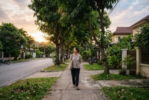 Một người đi bộ chậm trên vỉa hè rợp cây vào chiều muộn, không đeo tai nghe, tập trung vào nhịp thở